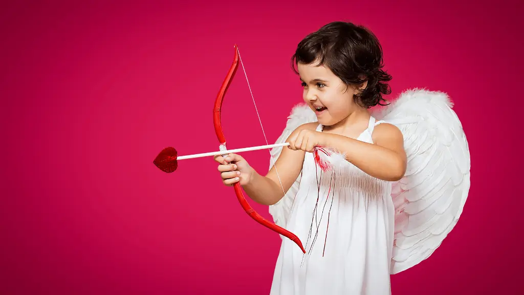 Criança vestida de anjo, com asas brancas e arco em formato de coração, simulando o cupido, sobre fundo rosa vibrante.