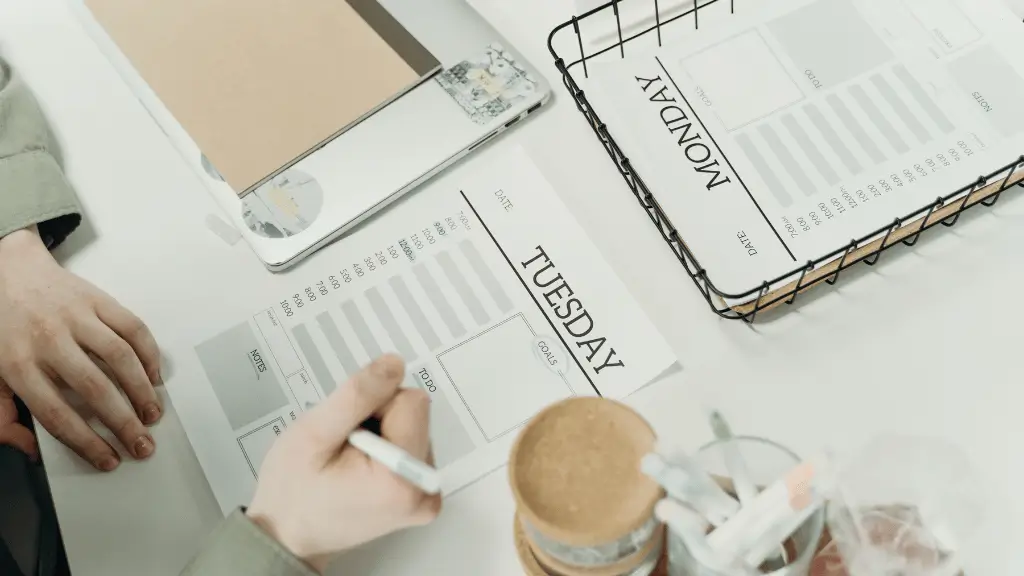 Pessoa escrevendo em uma agenda diária, com material de escritório organizado sobre a mesa, representando planejamento e organização